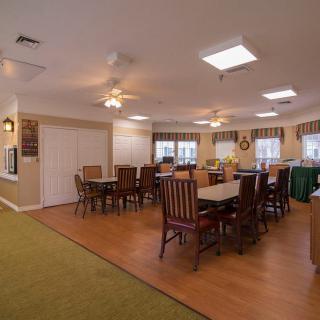 A spacious dining room with wooden tables and chairs, featuring ceiling lights and ample natural light.