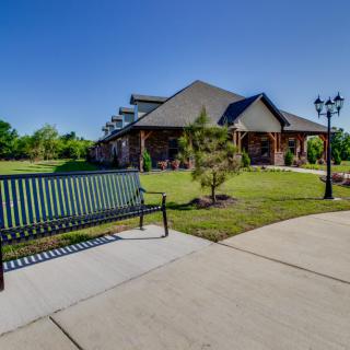 A sunny day at a park featuring a building, bench, and lush greenery.