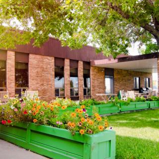 A cozy brick building with outdoor seating surrounded by vibrant flowers and greenery.