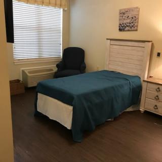A simple bedroom with a single bed, chair, and window.