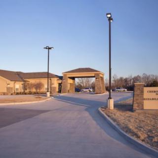 A view of a building entrance with a driveway and lamp posts.