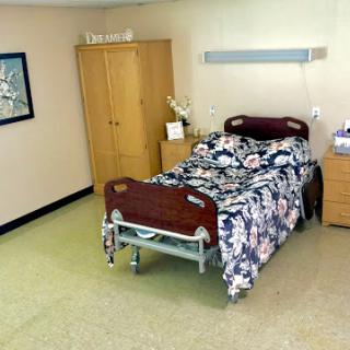 A view of a hospital room featuring a bed with floral sheets, a wardrobe, and nightstand.