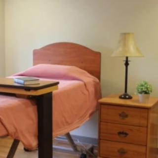 A cozy bedroom with a single bed and nightstand adorned with a lamp and books.