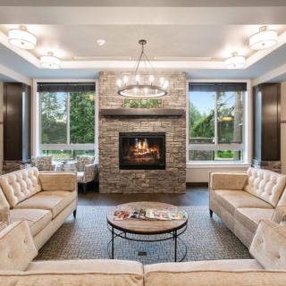 A modern living room featuring a central fireplace, elegant sofas, and a stylish coffee table with large windows providing natural light.