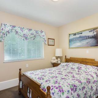 A cozy bedroom featuring a floral bedspread, wooden bed frame, and wall art with a window view.