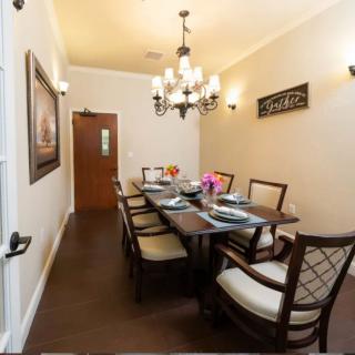 A neatly arranged dining room with a large wooden table, cushioned chairs, and an elegant chandelier.
