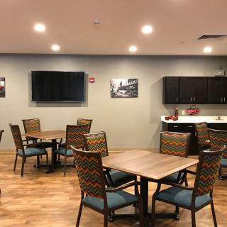A modern dining area with several tables, chairs, a television, and a kitchenette.