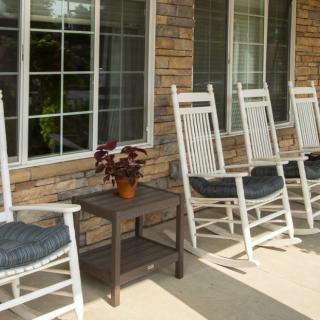 A row of rocking chairs on a porch with a small table and potted plant.
