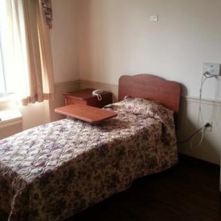 A simple room featuring a single bed with a floral quilt, positioned near a window with curtains.