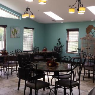 A brightly lit dining room with multiple tables and chairs, featuring decorative elements and large windows.