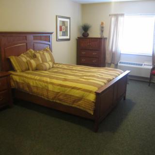 A neatly arranged bedroom with a large bed, dresser, and carpeted floor.