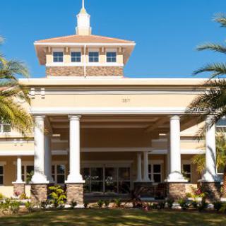 A sunny view of a building entrance featuring columns and palm trees.
