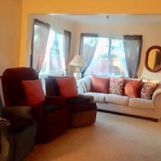A cozy living room featuring a sofa with decorative pillows, armchairs, and large windows with curtains.