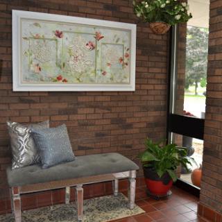 A cozy corner featuring a stylish bench, decorative artwork, and greenery against a rustic brick wall.