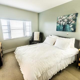 A cozy and inviting bedroom featuring a queen bed, elegant floral artwork, and plenty of natural light.