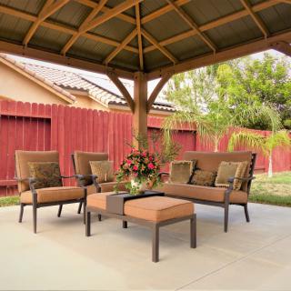 A cozy outdoor seating area under a wooden gazebo, featuring cushioned chairs and a coffee table, set against a landscaped backyard.
