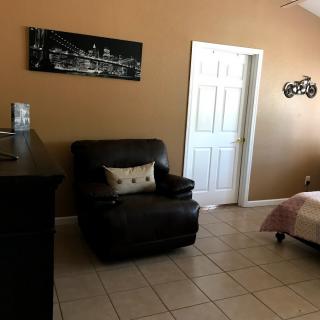 A cozy living room featuring a black armchair with a decorative pillow, complemented by wall art and tile flooring.