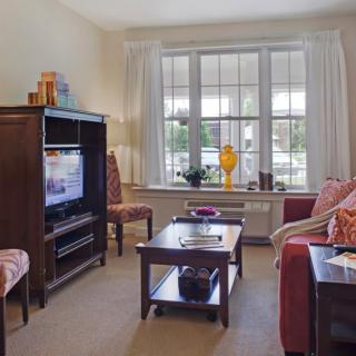A cozy living room with a sofa, coffee table, and television, featuring large windows and tasteful decor.
