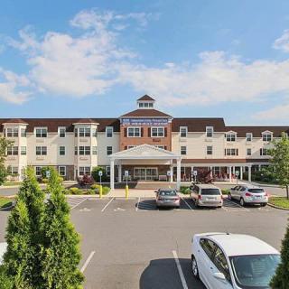 A three-story building with a parking lot in front, surrounded by trees under a partly cloudy sky.