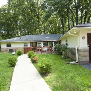A suburban house with a pathway leading to the entrance, surrounded by a grassy yard and trees.