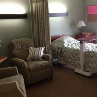 A hospital room featuring a bed, chairs, and a lamp with curtains for privacy.