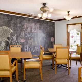 A cozy dining room featuring a large chalkboard wall, wooden tables, and cushioned chairs.