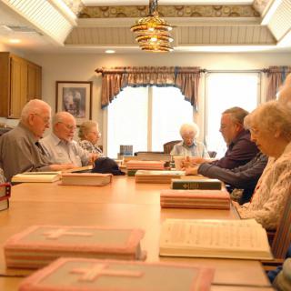 A group of seniors engaged in a meeting around a conference table surrounded by books.