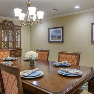 A neatly arranged dining room with a wooden table set for four, under a decorative chandelier.