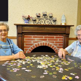 Two elderly women enjoying a puzzle together in a cozy indoor setting.