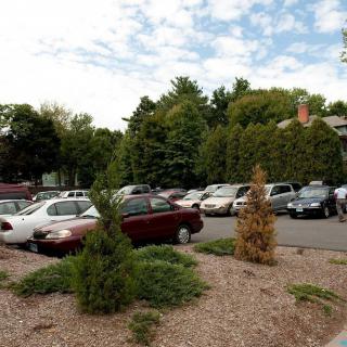 A parking lot filled with cars surrounded by trees and greenery under a partially cloudy sky.