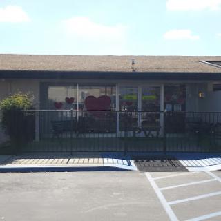 A view of a storefront with large windows and a parking area in front.