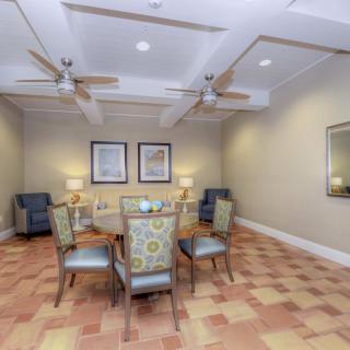A cozy dining room with a glass table and upholstered chairs, complemented by ceiling fans and framed artwork on the walls.
