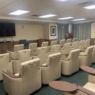 A spacious conference room with multiple rows of comfortable chairs facing a television.
