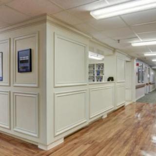 A well-lit hallway features a wooden floor and a reception area with decorative wall paneling.