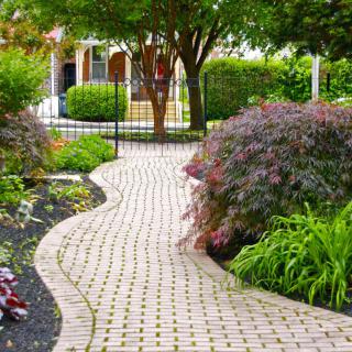 A beautifully landscaped garden featuring a winding brick pathway surrounded by lush plants and shrubs.
