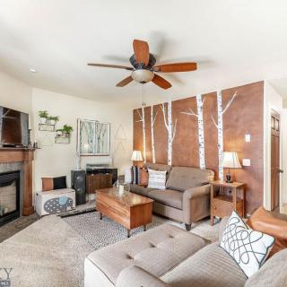 A cozy living room featuring a sofa, coffee table, and a fireplace with decorative wall art and a ceiling fan.