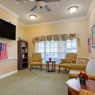 A cozy living room with armchairs and a TV, featuring flag decor and a window with curtains.