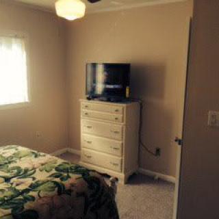 A cozy bedroom with a television on top of a dresser, next to a bed and window.