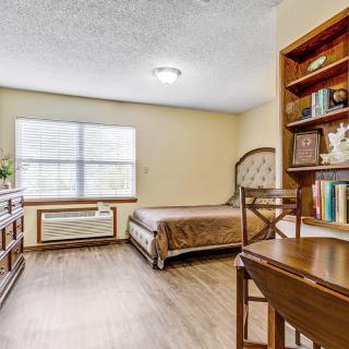 A cozy bedroom with a bed, bookshelf, desk, and window.