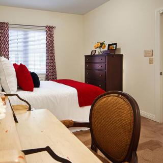 A cozy bedroom with a bed adorned with red and white linens, wooden dresser, and decorative curtains.