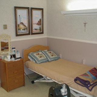 A small hospital room with a single bed, bedside table, and wall decor.