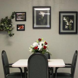 A dining area with a table and chairs, decorated with a flower arrangement and framed artwork on the wall.