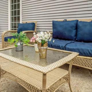 A cozy outdoor seating area with wicker furniture and blue cushions, adorned with potted plants and flowers on a glass-topped table.