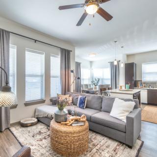 A modern open-concept living room with a comfortable sofa, wicker coffee table, and adjoining kitchen area.