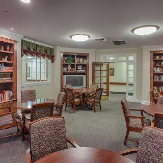 A cozy library room with bookshelves, tables, and chairs designed for reading and study.