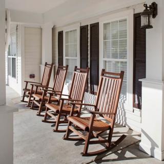 A sunny porch featuring several wooden rocking chairs lined up in front of large windows.