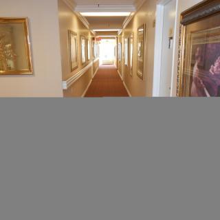 A well-lit hallway adorned with framed paintings along the walls.