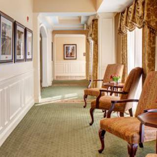 A well-lit hallway with elegant chairs, framed pictures, and ornate curtains.