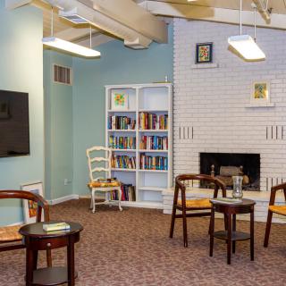 A cozy reading area with bookshelves, chairs, and a fireplace.