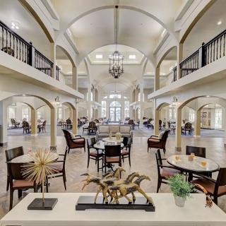 A spacious and elegantly designed interior with a dining area, featuring high ceilings, chandeliers, and decorative arches.